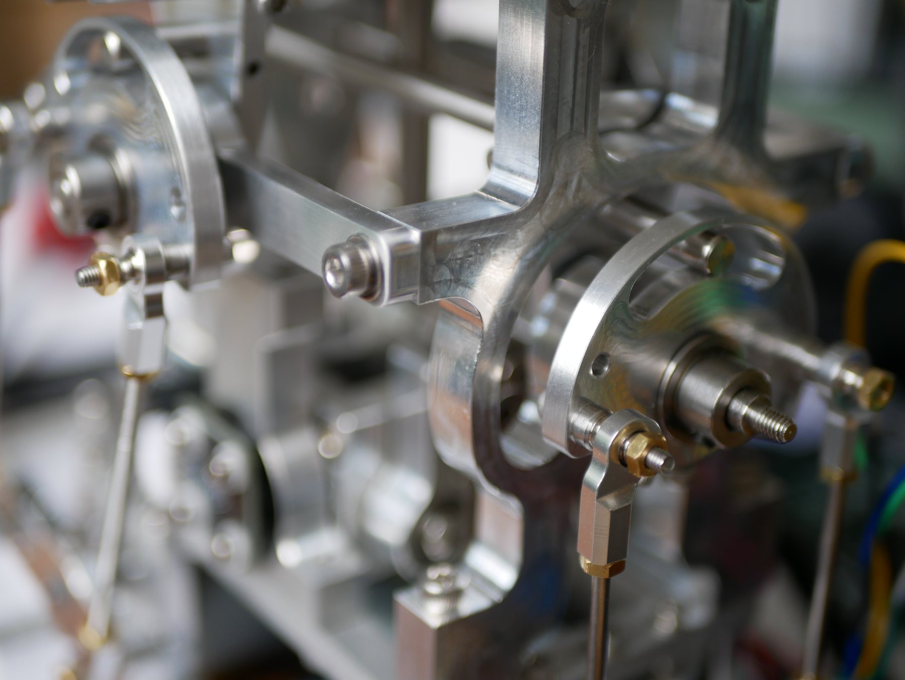 Macro detail of the device's frame and linkages: brushed aluminium brackets, brass fasteners, and stainless rod ends.